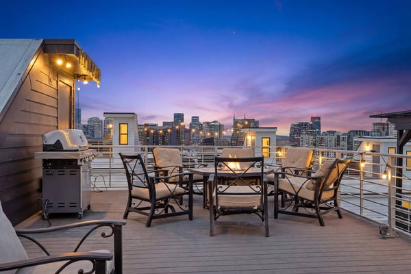 Modern rooftop deck with fire pit and city skyline at dusk, illuminated windows and downtown buildings in background