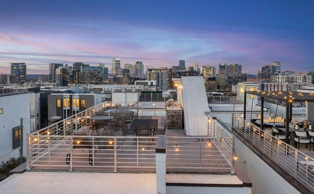 Rooftop terrace with lounge seating and city skyline at dusk, string lights and metal railings